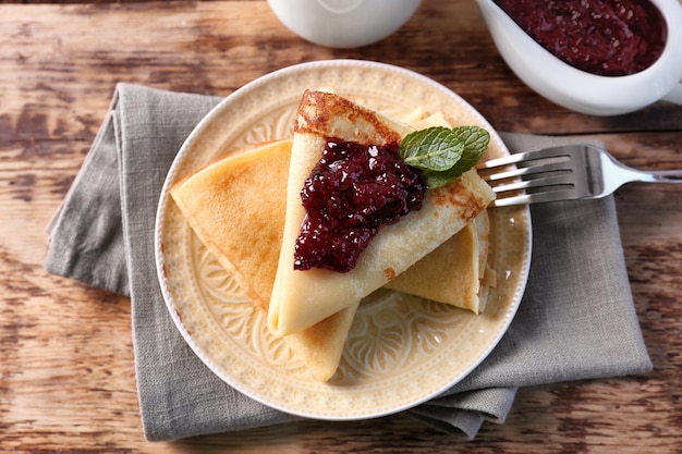 Placa con deliciosos panqueques y mermelada de bayas en la mesa