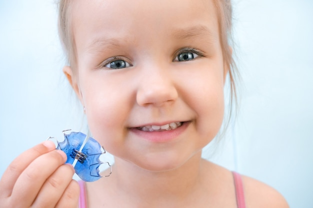 Placa dental. Expansión de la mandíbula en un niño. Un plato al cielo. No hay suficiente espacio para los molares. Niña feliz sosteniendo una placa de ortodoncia en sus manos