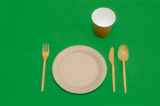Placa e copo de faca de colher de garfo reciclável em um fundo verde utensílios de cozinha vista superior