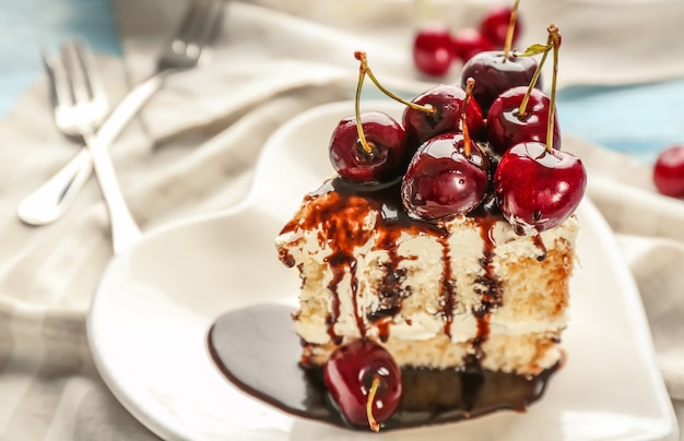 Placa en forma de corazón con un trozo de delicioso pastel de cerezas en la mesa