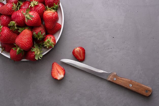 Placa con fresas maduras y cuchillo sobre fondo de hormigón gris, concepto de verano, de cerca.