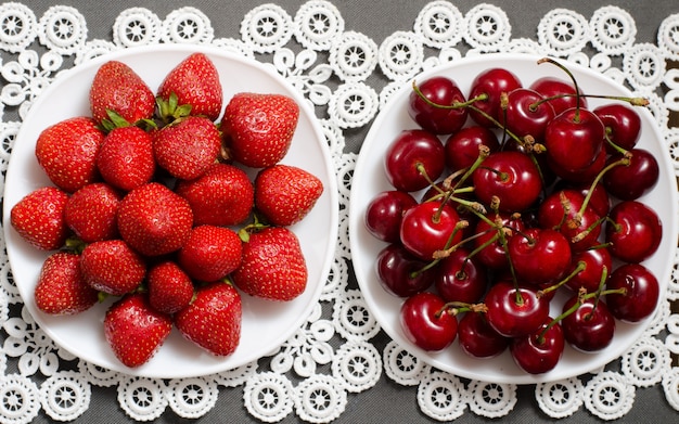 Placa con fresas y un plato de cerezas rojas en una servilleta de encaje, vista superior
