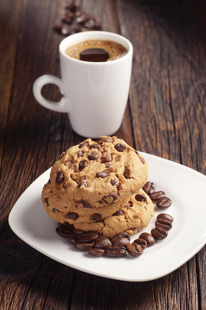 Placa con galletas de chocolate y taza de café en la mesa de madera oscura.