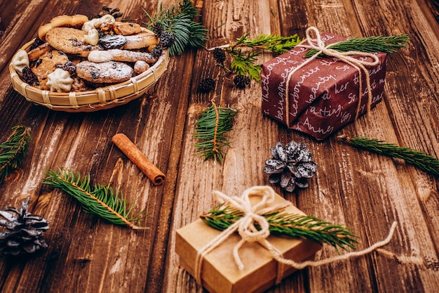 Placa con galletas de Navidad se encuentra en la mesa con regalos, ramas de abeto y conos