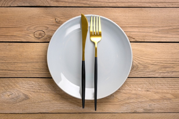 Placa gris con tenedor y cuchillo sobre mesa de madera