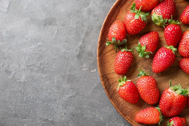 Placa de madera con fresas frescas sobre fondo gris