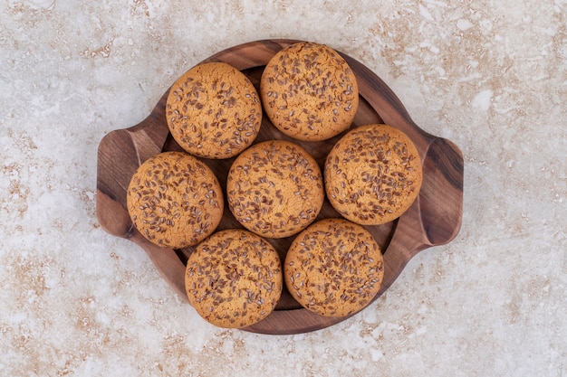 Placa de madera llena de galletas de avena en la superficie de mármol.