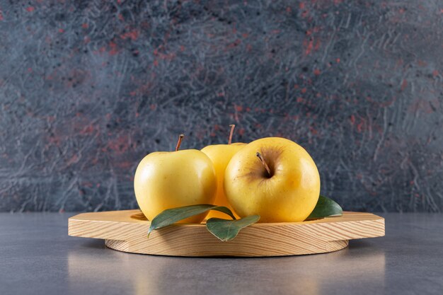 Placa de madera de manzanas amarillas con hojas verdes sobre piedra.