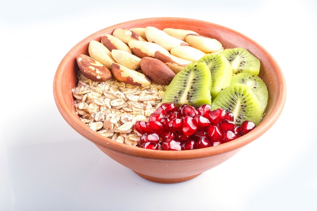 Una placa con muesli, kiwi, granada, nueces de Brasil aisladas sobre fondo blanco.