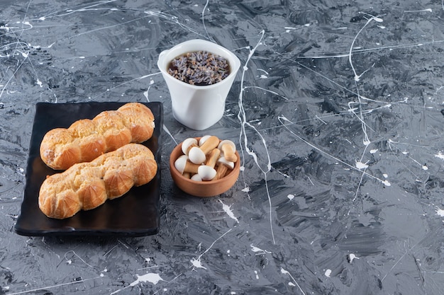 Placa negra de bollos de crema y taza de té en la mesa de mármol.