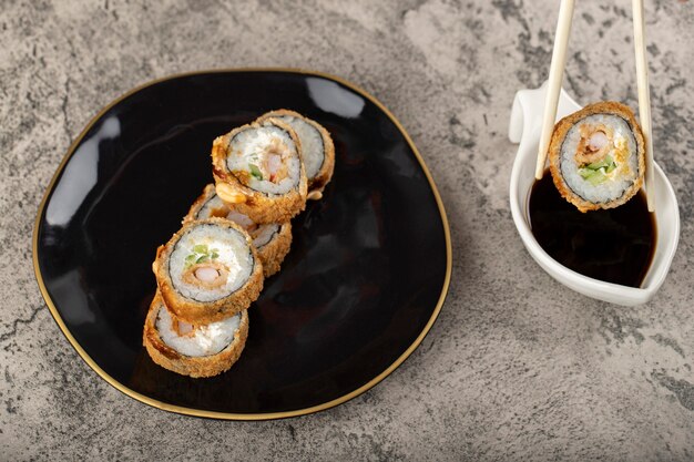 Placa negra de rollos de sushi con salsa de soja colocada sobre una mesa de piedra.