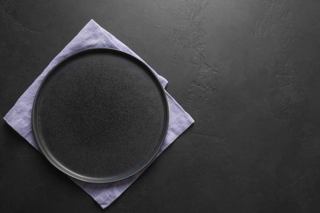 Placa negra vacía con una toalla lila sobre fondo negro de cocina. Espacio para el diseño. Vista desde arriba.