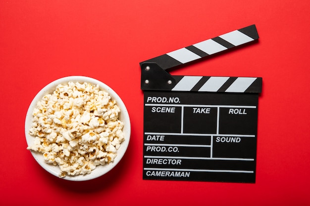 Placa con palomitas de maíz y claqueta de cine sobre un fondo rojo.