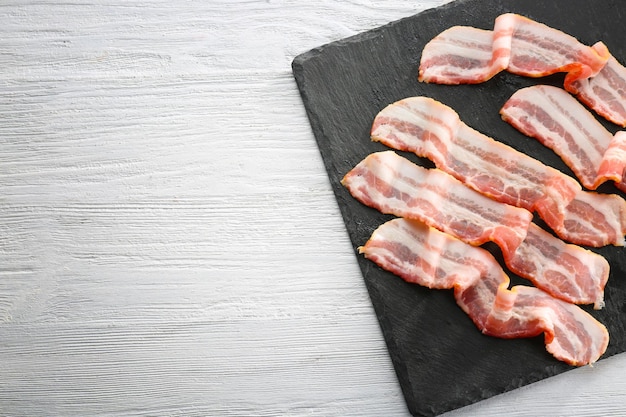 Placa de pizarra con tiras de tocino sobre mesa de madera