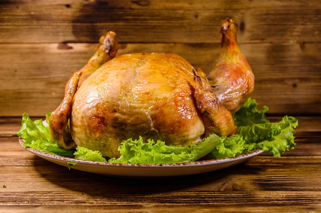 Placa con pollo entero asado y hojas de lechuga sobre una mesa de madera