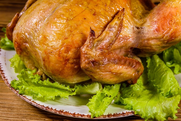 Placa con pollo entero asado y hojas de lechuga sobre una mesa de madera