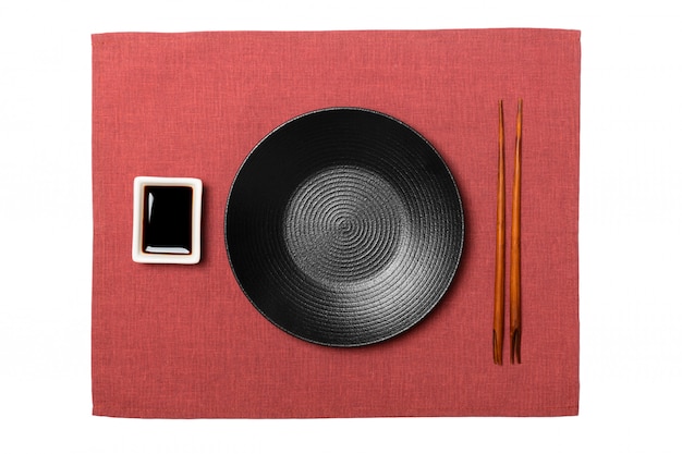 Placa preta redonda vazia com pauzinhos para sushi e molho de soja, guardanapo vermelho. vista superior com copyspace