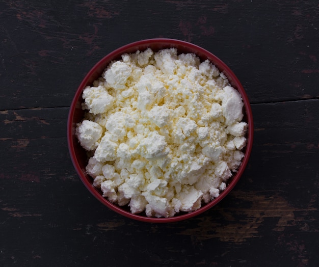 Placa roja con cuajada de leche blanca sobre la vieja mesa de madera negra.