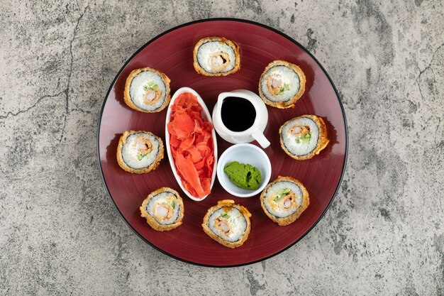 Placa roja de rollos de sushi calientes colocados sobre la mesa de piedra.
