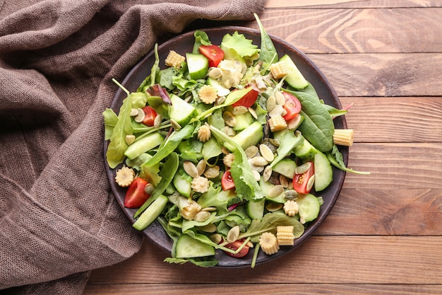 Placa con sabrosa ensalada de verduras sobre fondo de madera