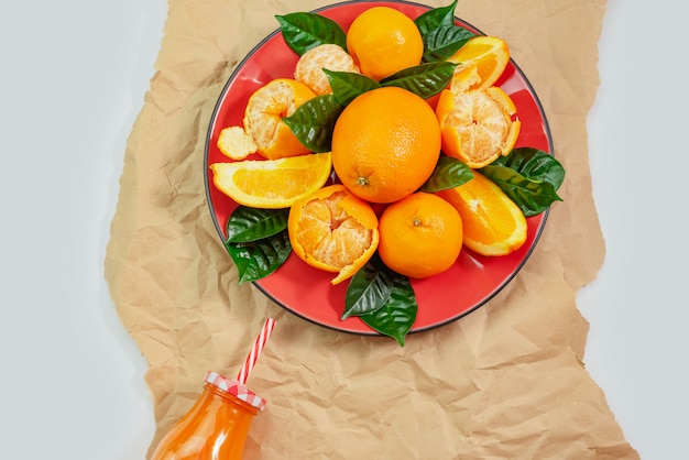 Placa vermelha com laranjas e tangerinas verdes folhas garrafa com suco de luz de fundo Vista superior cópia espaço