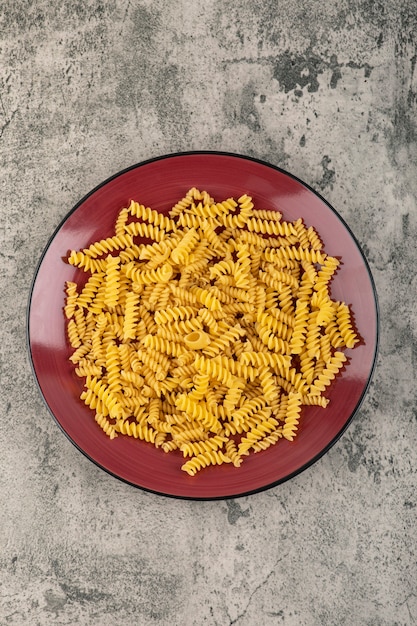 Placa vermelha de massa fusilli crua na mesa de pedra.