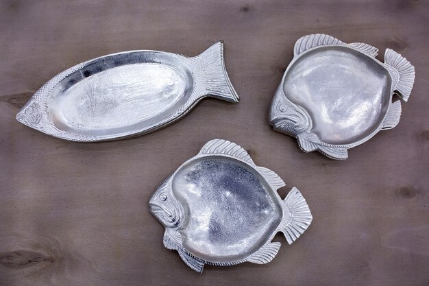 Placas de plata vacías con forma de pez sobre una mesa de madera