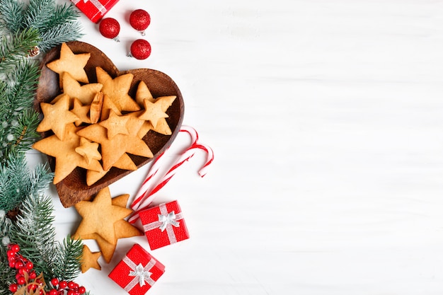 Plätzchen, Geschenke und Tannenbaumaste auf einem weißen Holztisch.