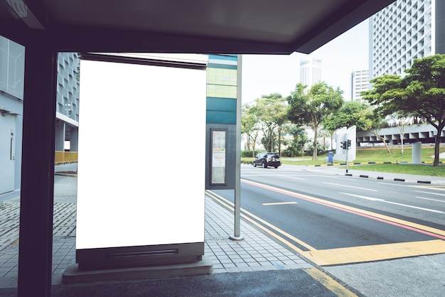 Plakat an der Bushaltestelle mit leeren Werbebanner auf sonnenbeschienenen Straße.