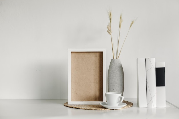 Plakatkunstmodell mit Holzrahmen, getrocknetem Gras in Vase, Tasse Kaffee und Büchern, Boho-Interieur