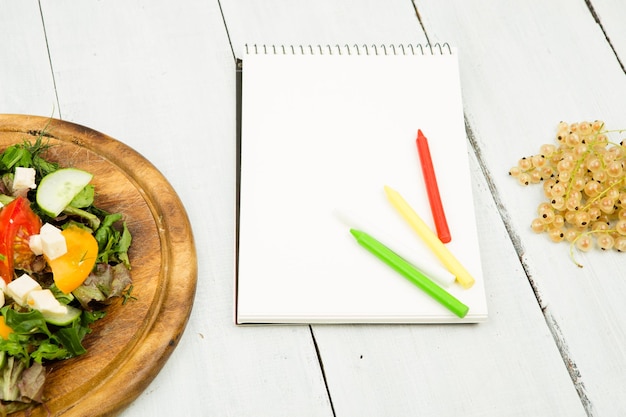 Plan de dieta una ensalada de verduras frescas y un cuaderno en blanco sobre una mesa de madera blanca