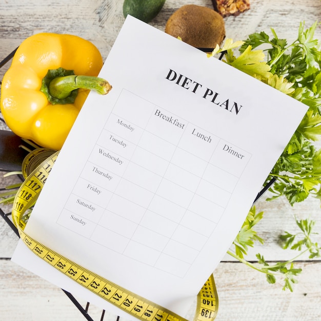 Foto plan de dieta envuelto con cinta métrica sobre verduras frescas