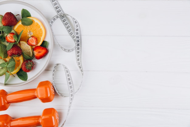 Foto plan de dieta, menú o programa, cinta métrica, agua, pesas y comida dietética de frutas frescas en blanco