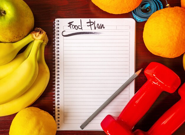 Foto plan de dieta. plan de dieta y frutas y pesas sobre una superficie de madera