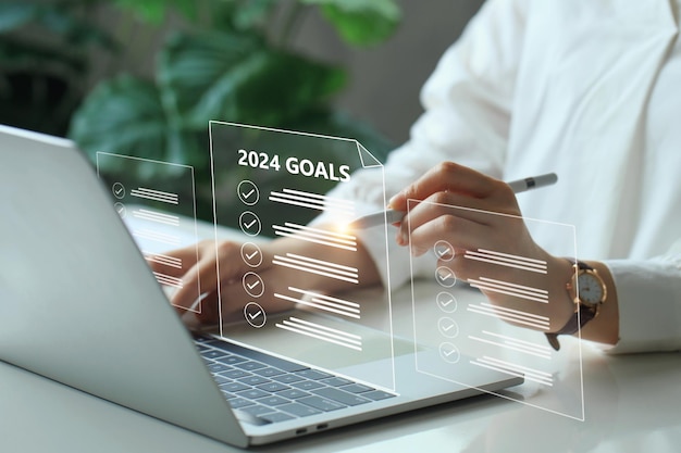 Foto plan de metas de año nuevo 2024 y conceptos de acción mujer de negocios usando una computadora portátil con una meta virtual 2024