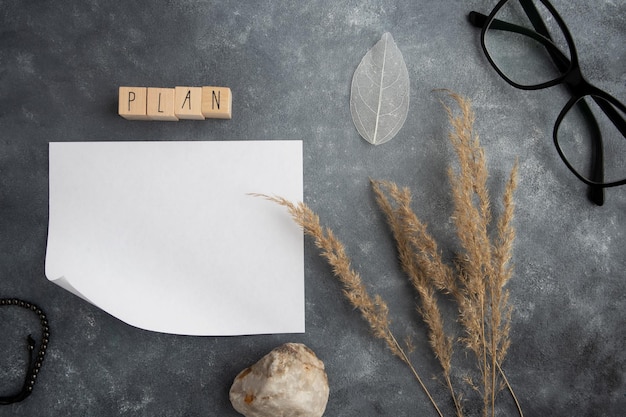 Plan de palabras en papel en blanco sobre cubos de madera, hierba de pampa y piedra sobre un fondo gris con espacio para el texto