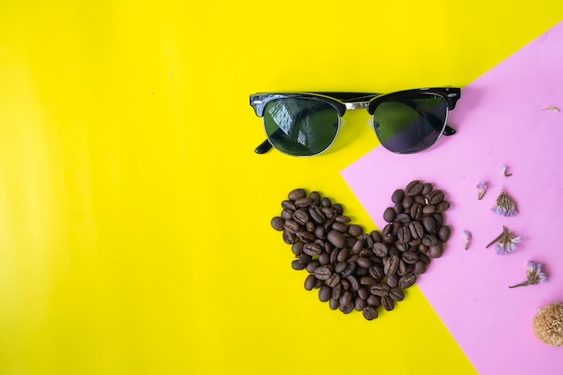 plana pone granos de café en forma de corazón con gafas de sol sobre fondo dulce dos tonos