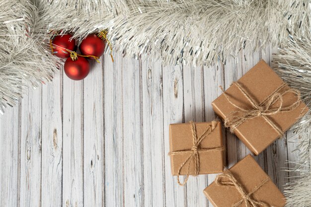 Plana pone tres cajas de regalo en una mesa de madera decorada con una guirnalda y bolas rojas de navidad para el año nuevo o navidad. concepto de servicio de correo, mensajería o entrega. copia espacio