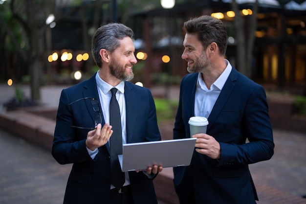 Planejamento de duas equipes de negócios com café para viagem e equipe de homens de negócios ao ar livre usando lapto