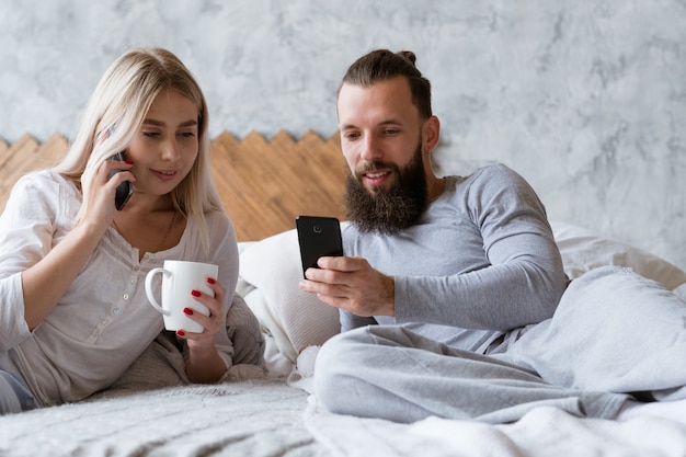 Planejamento do dia de trabalho pela manhã. Jovem e mulher na cama ligando e verificando o smartphone.