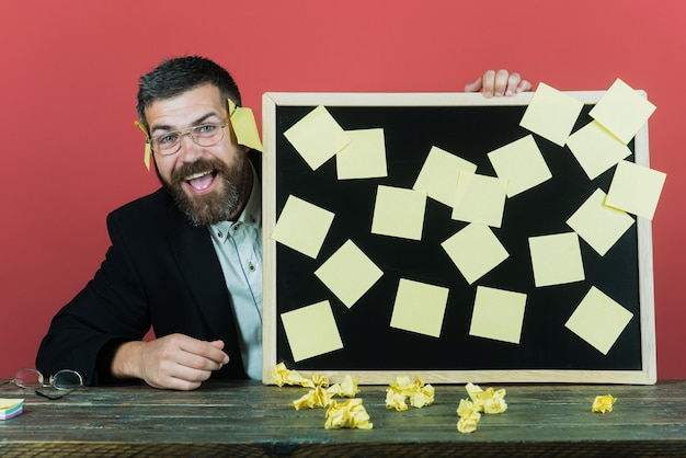 Planejamento. Gestão. Emprego. O negócio. Lembrete. Empresário mantém placa com notas de adesivos de memorando. Homem barbudo de óculos detém adesivo. Isolado em um fundo vermelho.