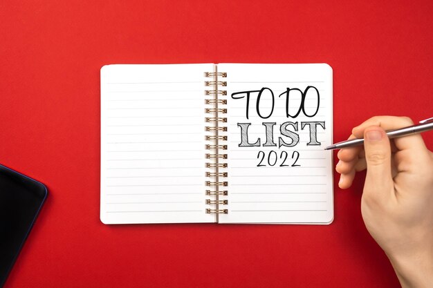 Planejamento para o conceito de ano novo 2022. Caderno com lista de tarefas. Fundo vermelho, caneta prateada, espaço de cópia e foto de vista superior