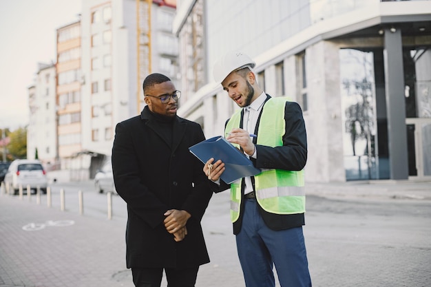 Planejando a casa. Homem de uniforme e cliente preto olhando para a nova planta da casa construída