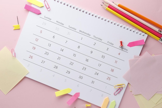 Planejando o calendário em um fundo rosa com alfinetes, lápis, adesivos ... Data importante. Lugar para texto. Conceito de planejamento.