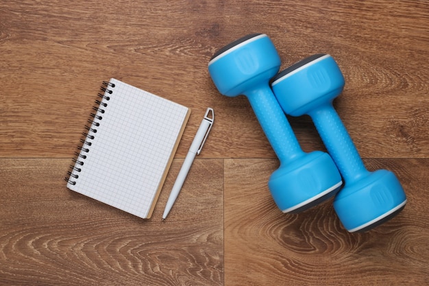 Planeje seus exercícios futuros. Elaboração de um programa de treinamento. Caderno com caneta e halteres no chão. Fitness, conceito de esporte.