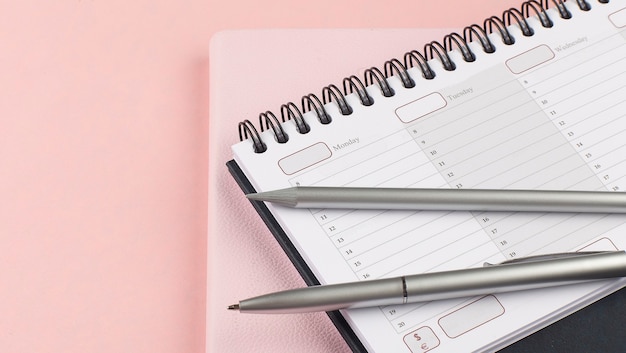 Planer mit Kugelschreiber und Bleistift auf rosa Hintergrund