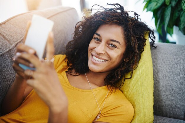 Los planes primero y luego me levantaré de este sofá Retrato en ángulo alto de una mujer joven atractiva que usa su teléfono celular mientras se relaja en casa el fin de semana