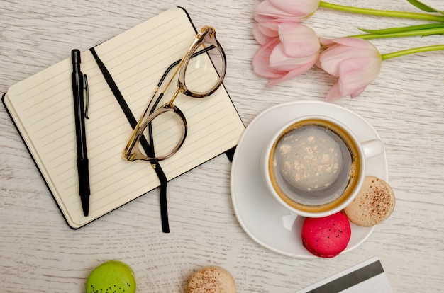 Planificación de asuntos. Taza de café con postre, cuaderno, bolígrafo y vasos.