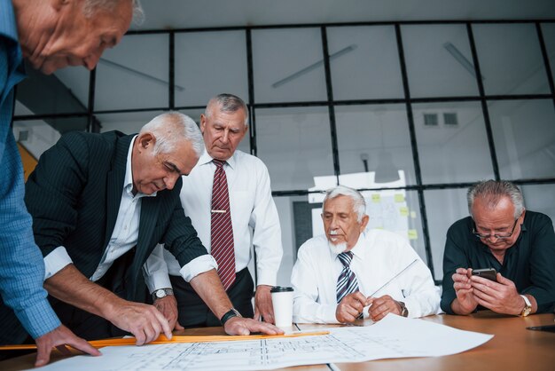 Planificación de la construcción midiéndola en papel. Equipo envejecido de arquitectos de negocios de edad avanzada tiene una reunión en la oficina.