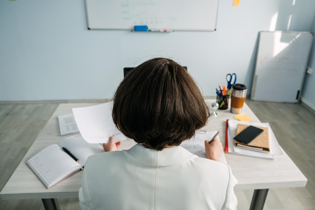 Planificación de la gestión del tiempo para gerentes de propietarios de negocios Gerente de joven empresaria sentada a la mesa en la oficina y tomando notas en el diario y el calendario